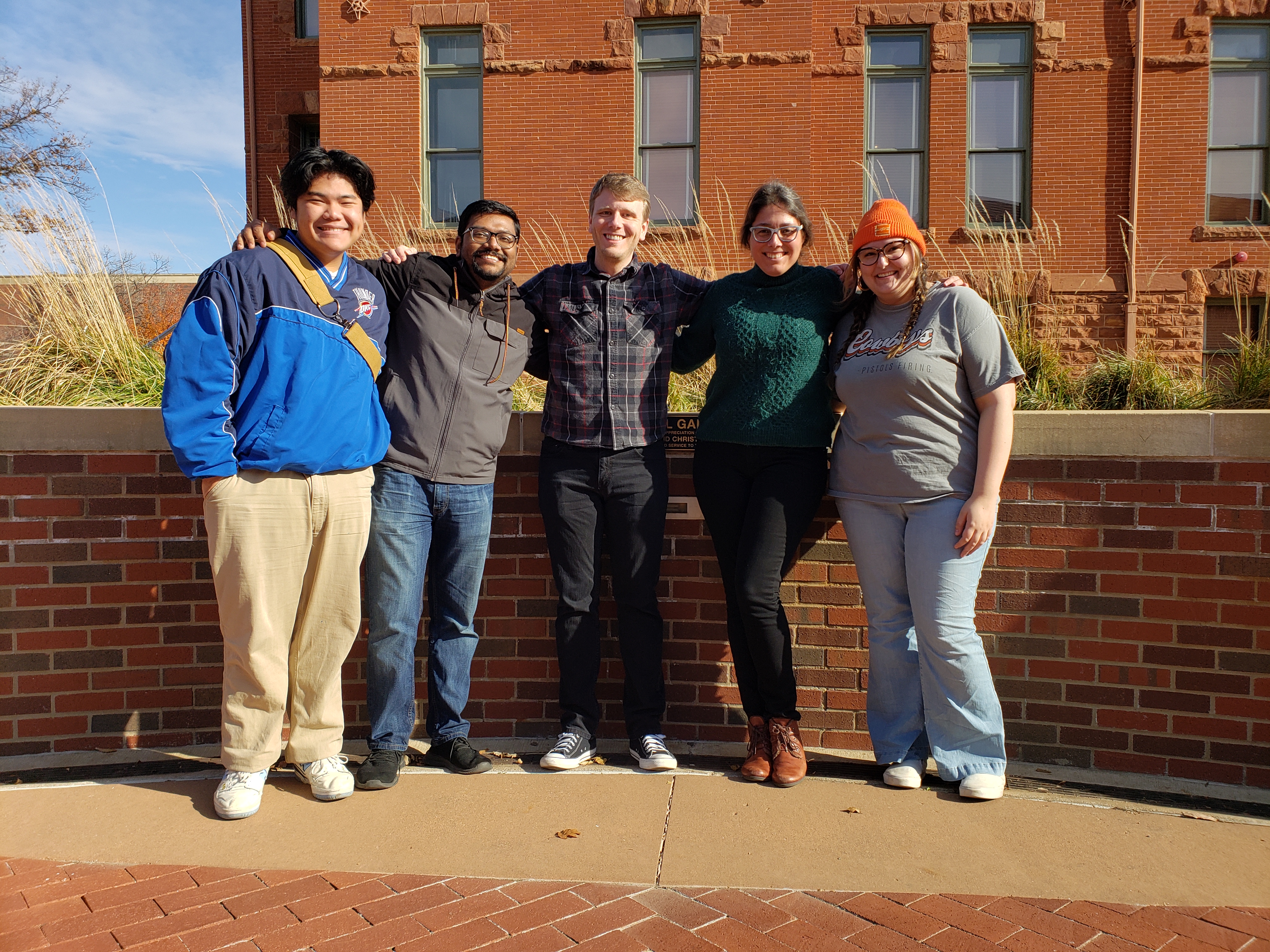 Photograph of Jonathan, Niladri, Reed, Mercedes, and Madeline standing together in front of a brick building on the Stillwater campus.